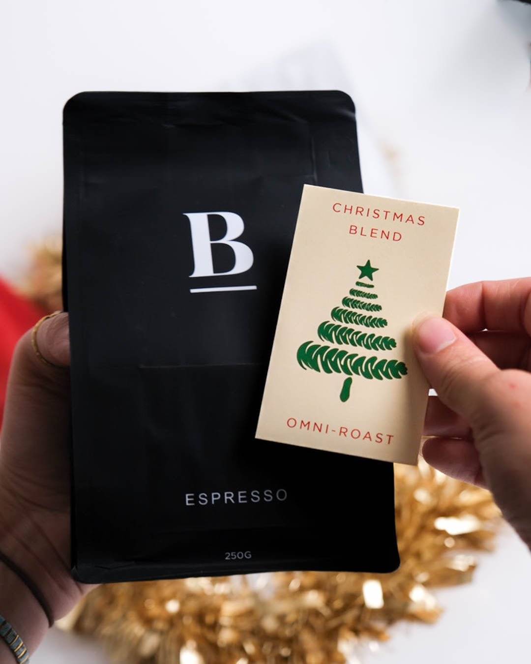 Black coffee bag with 'B' logo and a Christmas blend label held by a person.